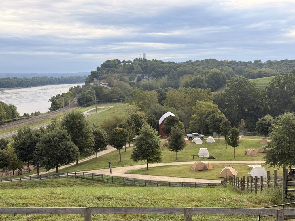 Tents on a green hillside above the Missouri River and the railroad, a red barn among the trees